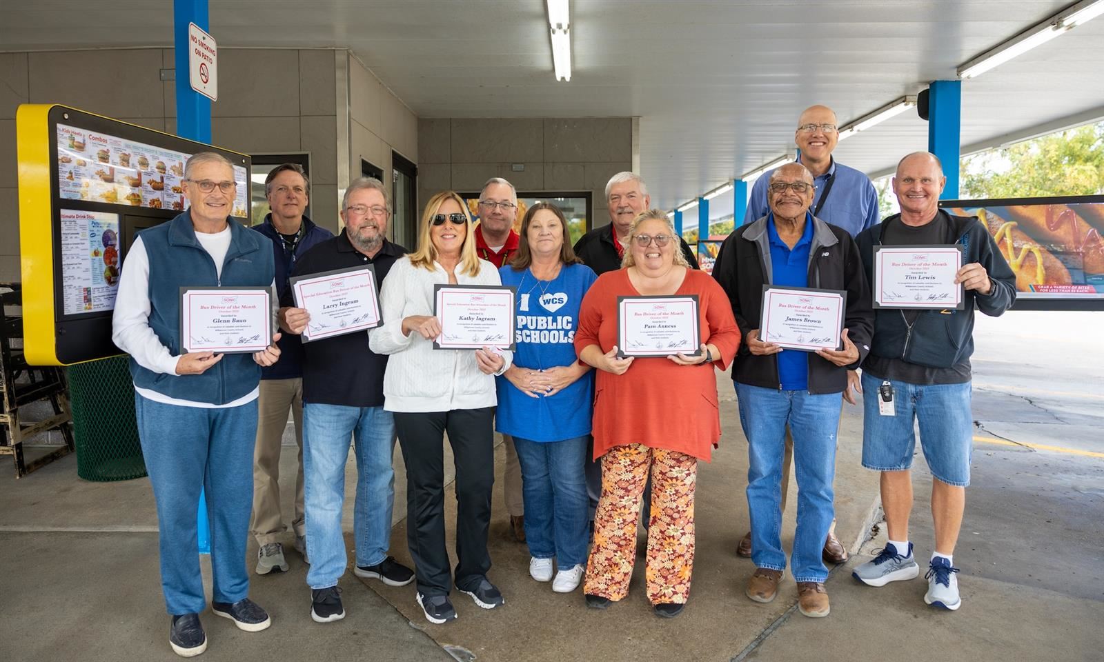 Bus drivers smile while holding certificates